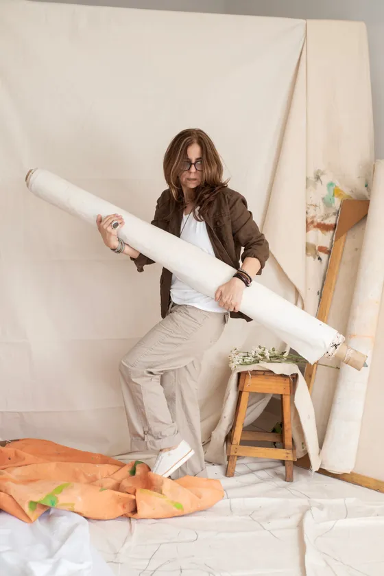 Elsa Basil carrying a rolled canvas in her studio